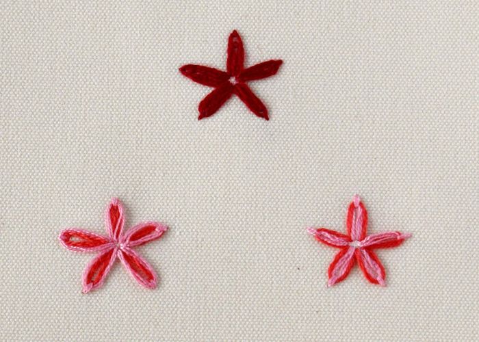 Tres flores bordadas con punto Lazy Daisy en colores rojo y rosa